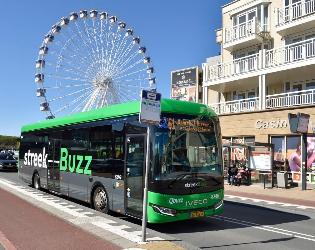 Een groene streekbus staat stil bij een halte in Katwijk. De bus staat voor een casino en een reuzenrad.