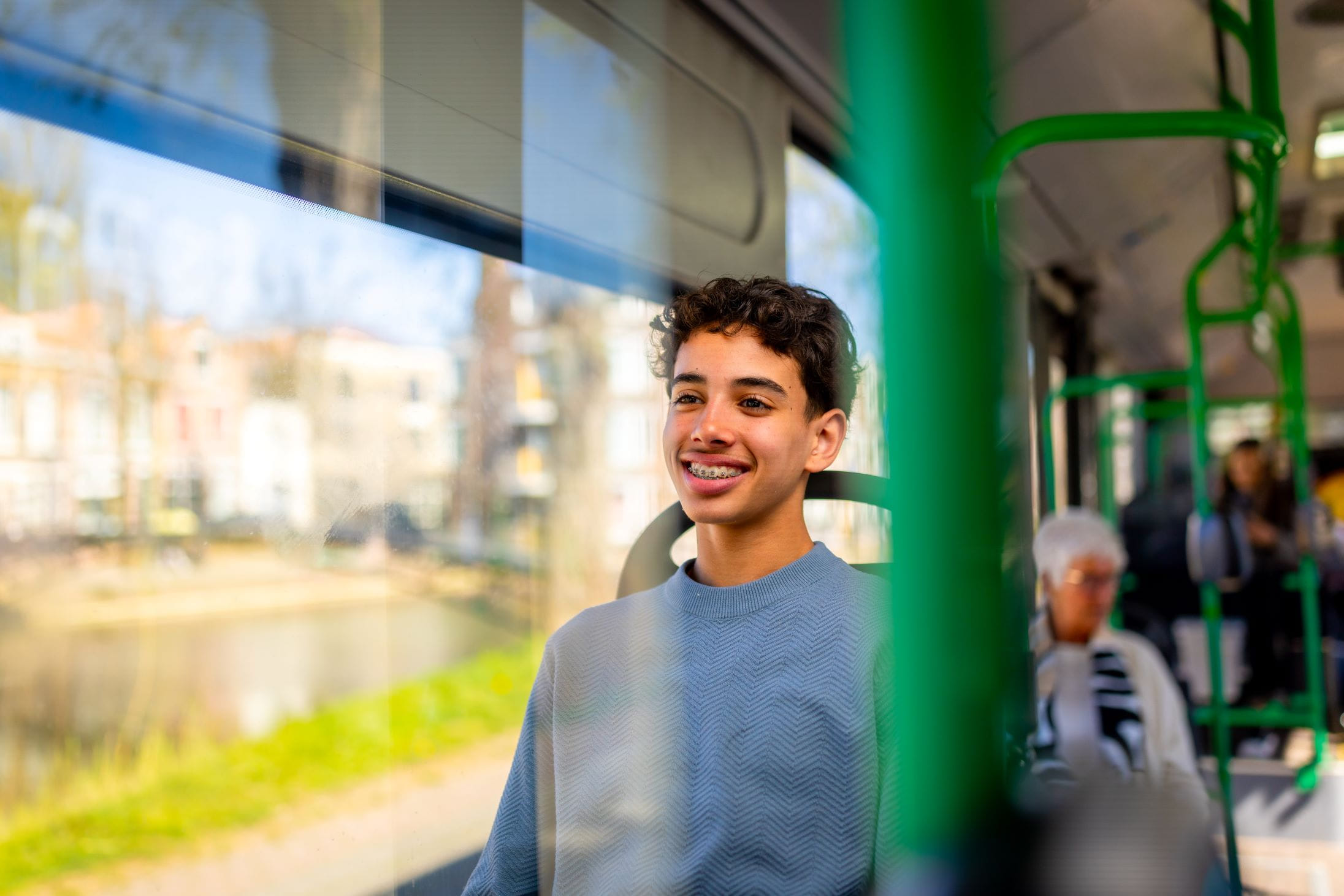 Jonge jongen met donker haar zit glimlachend in de bus aan de kant van het raam