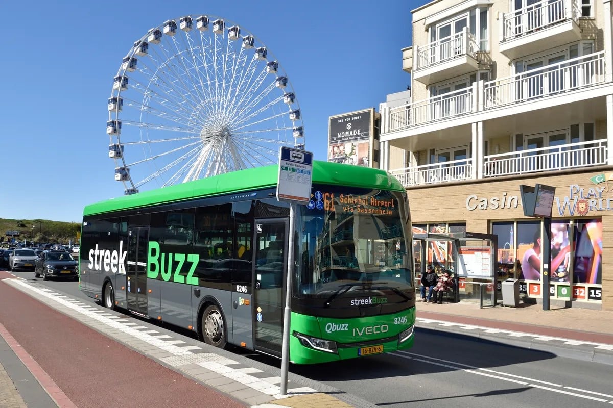 Een groene streekbus staat stil bij een halte in Katwijk. De bus staat voor een casino en een reuzenrad.